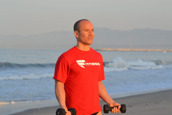 A man holding two dumbbells on the beach