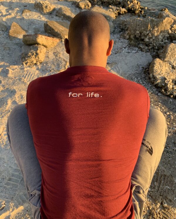 A man sitting on the ground wearing a red shirt