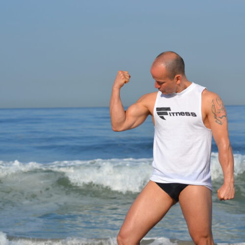 A man in his underwear is flexing muscles on the beach.