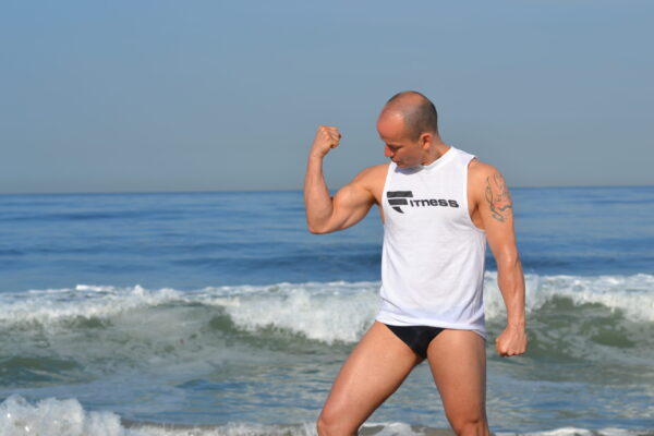 A man in his underwear is flexing muscles on the beach.