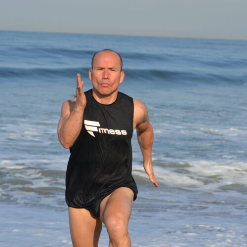 A man in black shirt and shorts standing on beach.