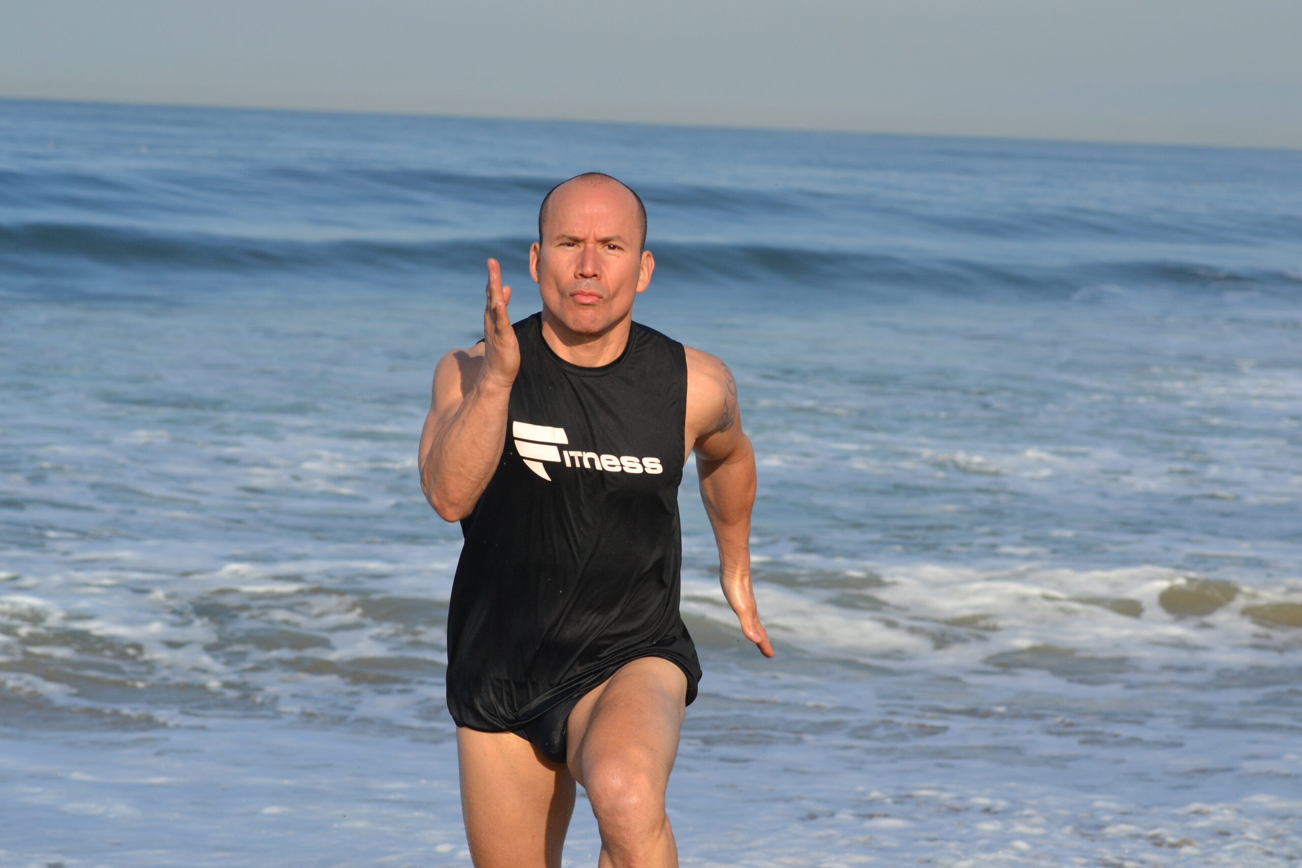 A man in black shirt and shorts standing on beach.